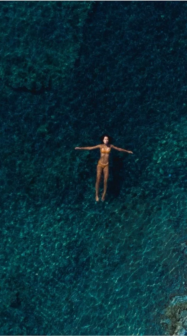 A swimmer floating face-up in dark green water, arms open.